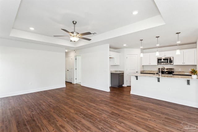 unfurnished living room featuring dark wood-style floors, ceiling fan, a raised ceiling, and baseboards