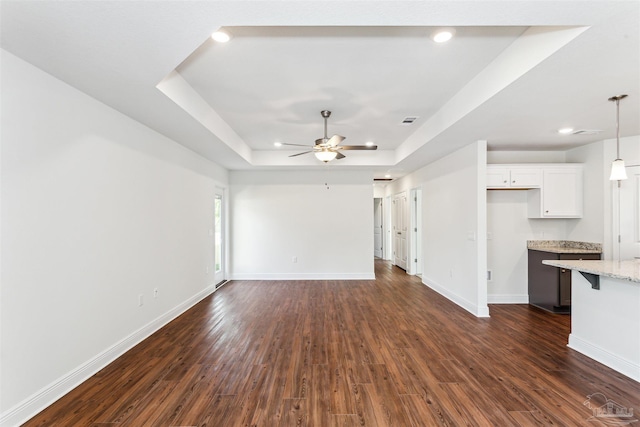 unfurnished living room with dark wood-style floors, a raised ceiling, and baseboards