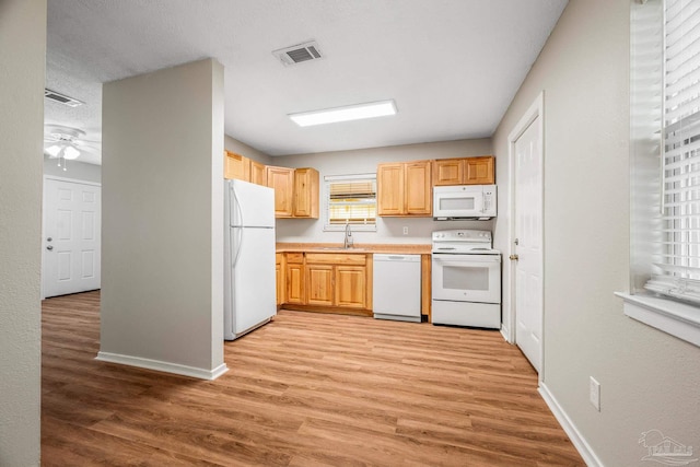 kitchen with light wood-style flooring, white appliances, a sink, visible vents, and light countertops