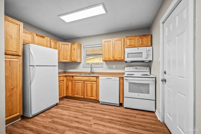 kitchen with white appliances, light wood finished floors, light countertops, light brown cabinets, and a sink