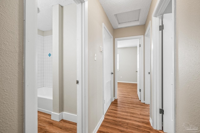 hall featuring attic access, a textured ceiling, baseboards, and wood finished floors