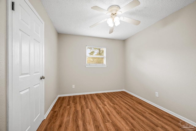 empty room with a textured ceiling, wood finished floors, a ceiling fan, and baseboards