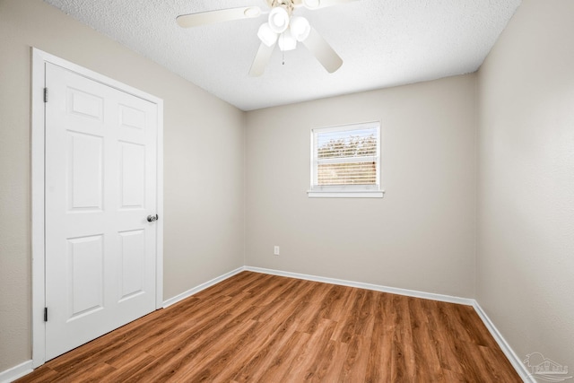 empty room featuring a textured ceiling, ceiling fan, wood finished floors, and baseboards