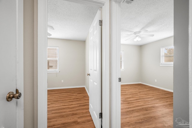 corridor featuring a textured ceiling, baseboards, and wood finished floors