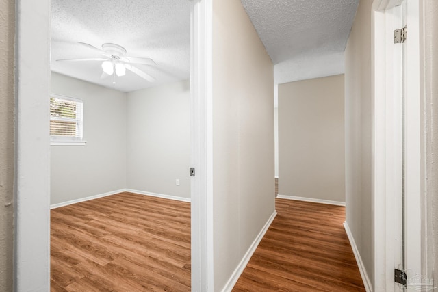 hall featuring a textured ceiling, baseboards, and wood finished floors