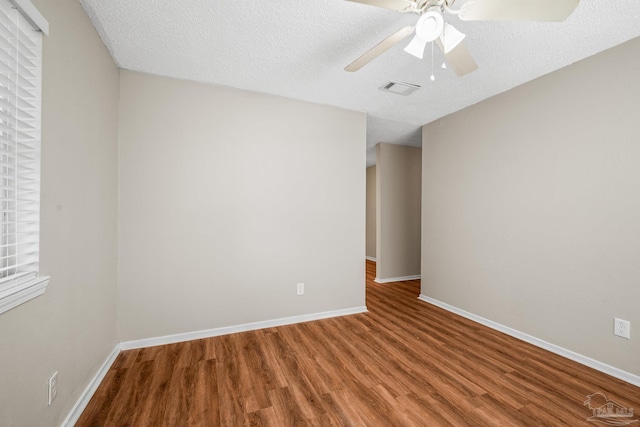 empty room featuring baseboards, visible vents, a ceiling fan, wood finished floors, and a textured ceiling