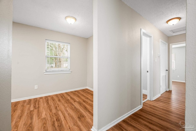 hall featuring a textured ceiling, baseboards, and wood finished floors