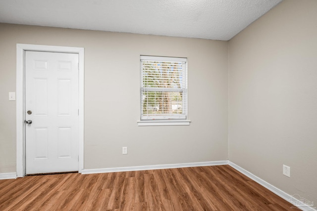 empty room with a textured ceiling, baseboards, and wood finished floors