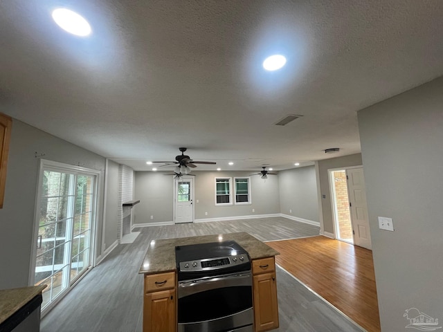 kitchen featuring a brick fireplace, ceiling fan, dark stone countertops, hardwood / wood-style floors, and stainless steel range with electric cooktop