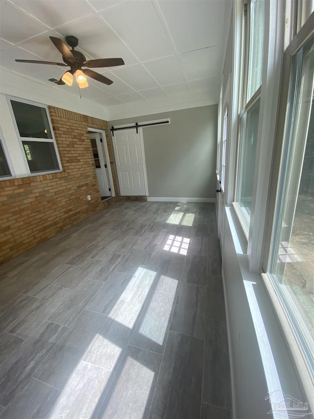 unfurnished room with a barn door, ceiling fan, and brick wall