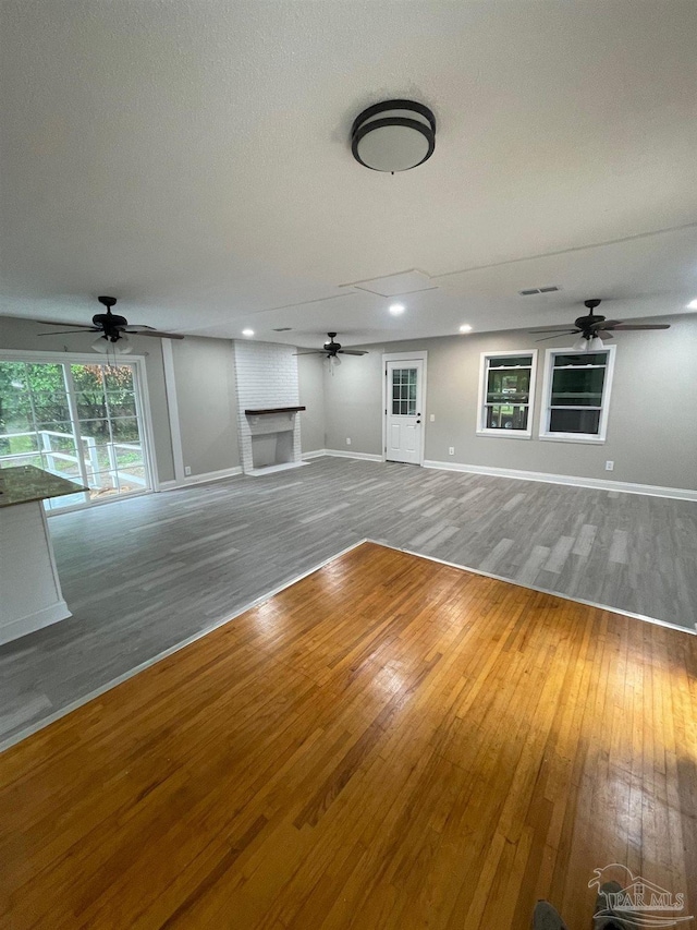 unfurnished living room with ceiling fan, wood-type flooring, and a fireplace