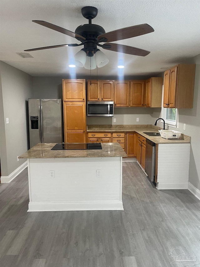 kitchen featuring appliances with stainless steel finishes, ceiling fan, sink, hardwood / wood-style flooring, and a kitchen island