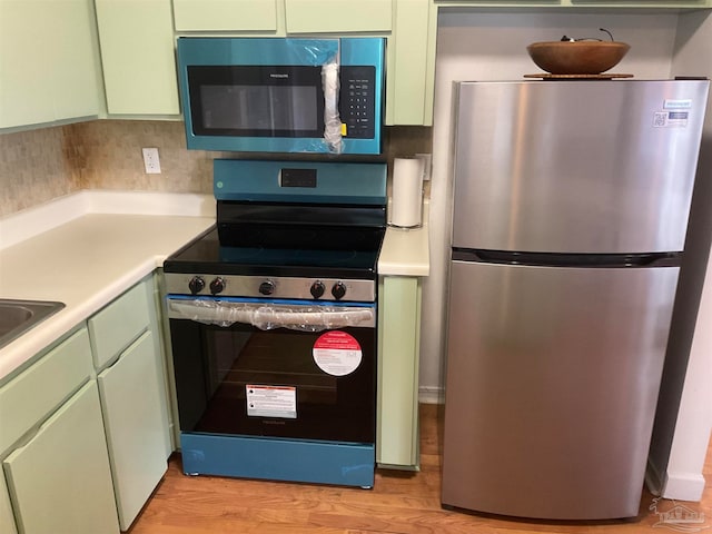 kitchen featuring green cabinets, light wood-type flooring, backsplash, and appliances with stainless steel finishes