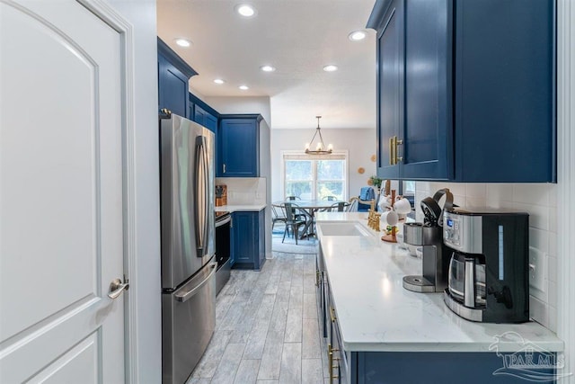 kitchen featuring blue cabinets, stainless steel appliances, light stone countertops, light wood finished floors, and tasteful backsplash