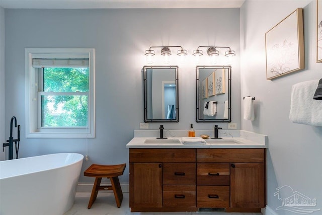 full bath with a freestanding bath, double vanity, a sink, and baseboards