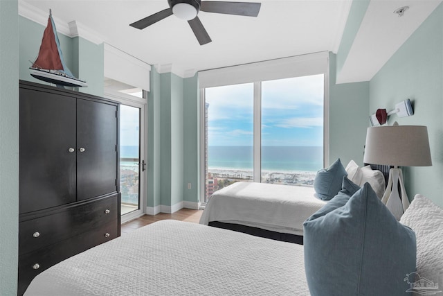 bedroom featuring a view of the beach, light hardwood / wood-style flooring, a water view, ornamental molding, and access to outside