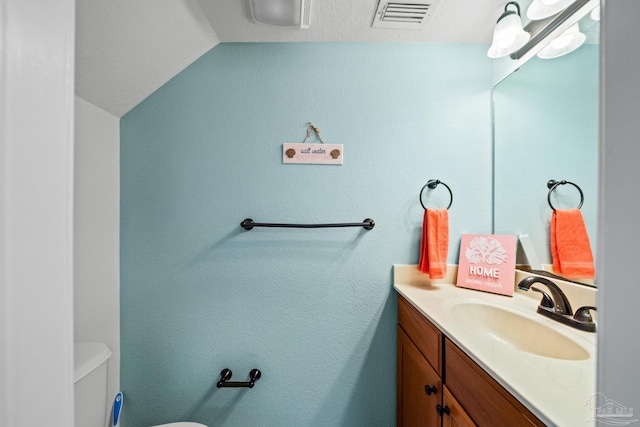 bathroom featuring visible vents, vanity, toilet, and lofted ceiling