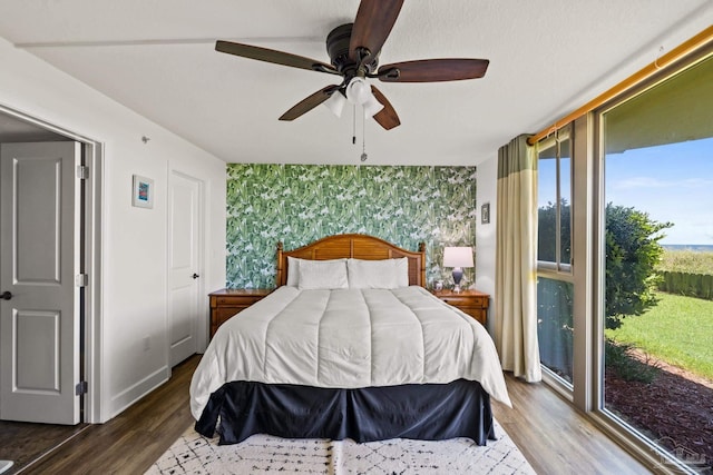 bedroom featuring an accent wall, dark wood-style flooring, baseboards, and wallpapered walls