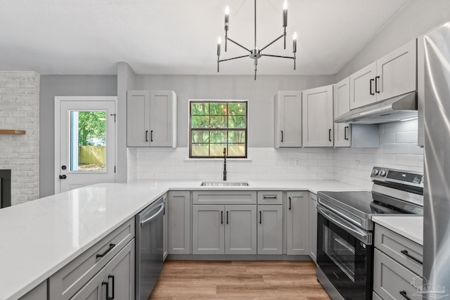 kitchen featuring gray cabinets, backsplash, appliances with stainless steel finishes, a sink, and under cabinet range hood
