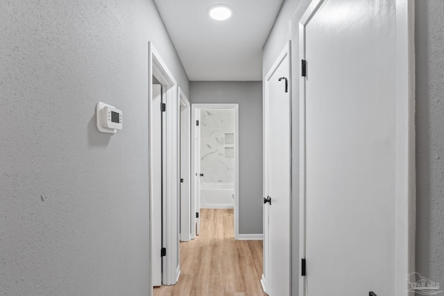 corridor featuring baseboards, a textured wall, and light wood-style flooring