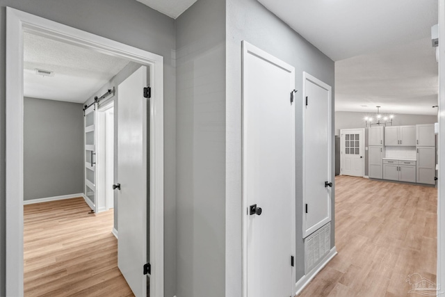 corridor with visible vents, a barn door, light wood-style flooring, and a notable chandelier
