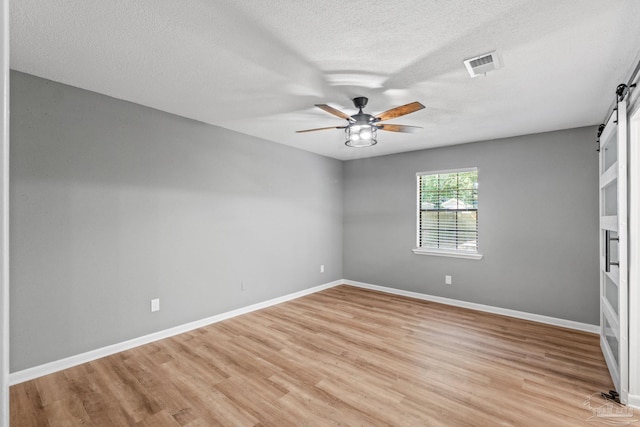 empty room featuring a ceiling fan, a textured ceiling, visible vents, light wood-type flooring, and a barn door