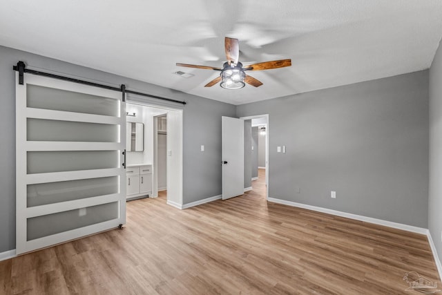 unfurnished bedroom with baseboards, light wood-type flooring, and a barn door