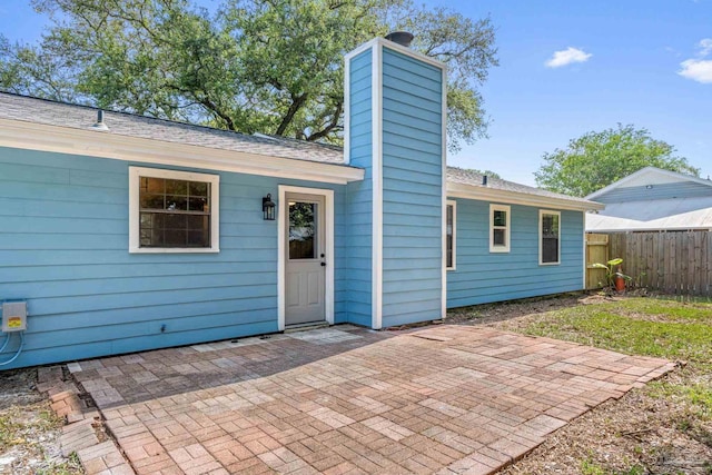 rear view of house featuring fence, a shingled roof, a chimney, and a patio area