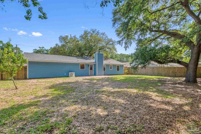 back of house featuring a yard, a chimney, and a fenced backyard