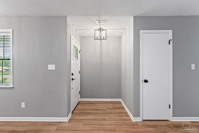 interior space with a textured ceiling, a notable chandelier, baseboards, and light wood-type flooring