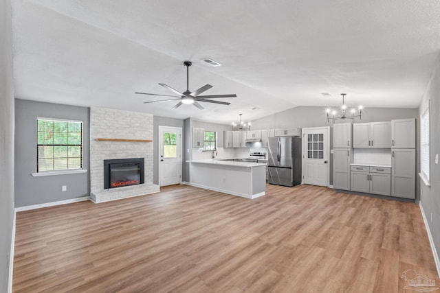 unfurnished living room with a healthy amount of sunlight, a fireplace, light wood-type flooring, ceiling fan with notable chandelier, and vaulted ceiling