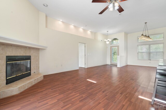 unfurnished living room featuring dark wood-type flooring, ceiling fan with notable chandelier, a fireplace, and a towering ceiling