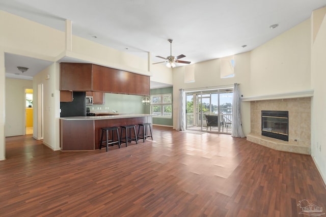 kitchen featuring a breakfast bar, black refrigerator, dark hardwood / wood-style floors, a tiled fireplace, and ceiling fan