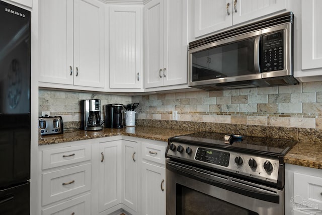 kitchen featuring appliances with stainless steel finishes, dark stone counters, and white cabinetry