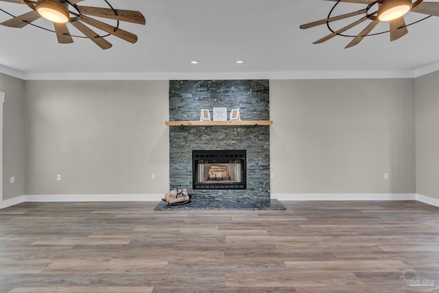 unfurnished living room featuring ceiling fan, ornamental molding, a stone fireplace, and hardwood / wood-style floors