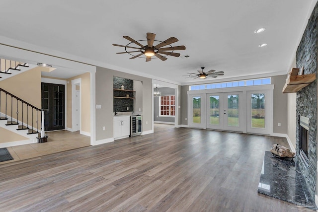 unfurnished living room with sink, ceiling fan, wine cooler, a fireplace, and light wood-type flooring