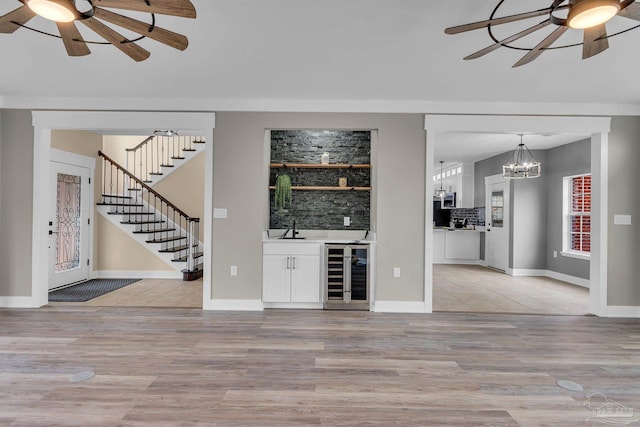 unfurnished living room featuring wine cooler, ceiling fan with notable chandelier, and light hardwood / wood-style flooring