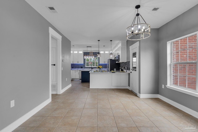 kitchen featuring stainless steel refrigerator, tasteful backsplash, white cabinets, decorative light fixtures, and a chandelier