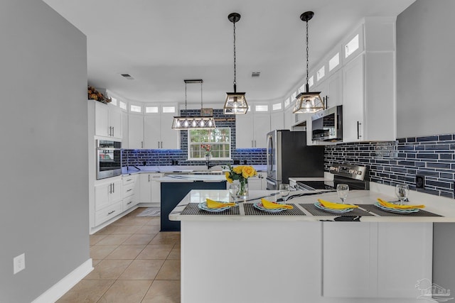 kitchen with light tile patterned floors, kitchen peninsula, a kitchen island, stainless steel appliances, and white cabinets