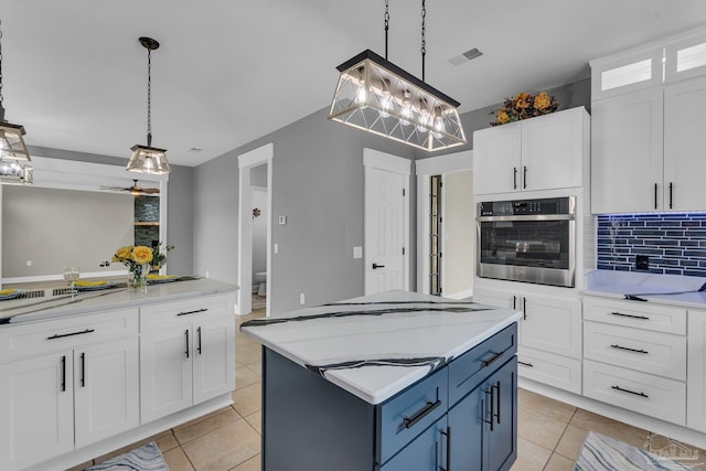 kitchen featuring stainless steel oven, decorative light fixtures, a kitchen island, and white cabinets