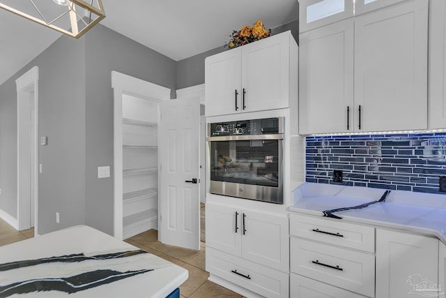 kitchen featuring backsplash, stainless steel oven, light tile patterned floors, and white cabinets