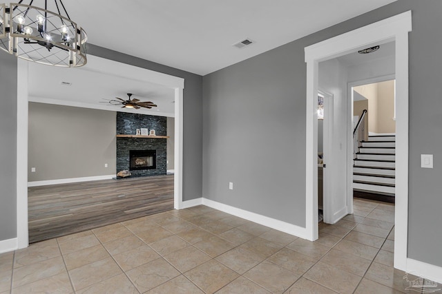 unfurnished living room featuring a stone fireplace, ceiling fan with notable chandelier, and light tile patterned floors