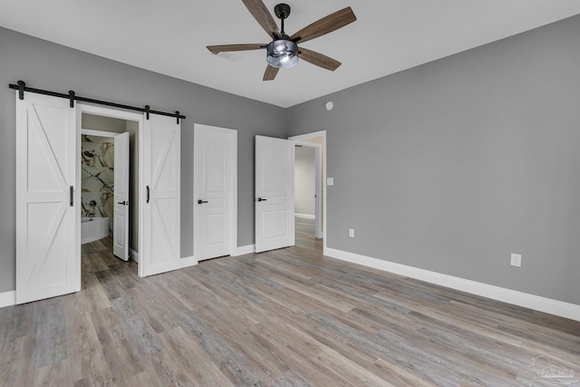 unfurnished bedroom with ceiling fan, ensuite bath, a barn door, and light hardwood / wood-style flooring