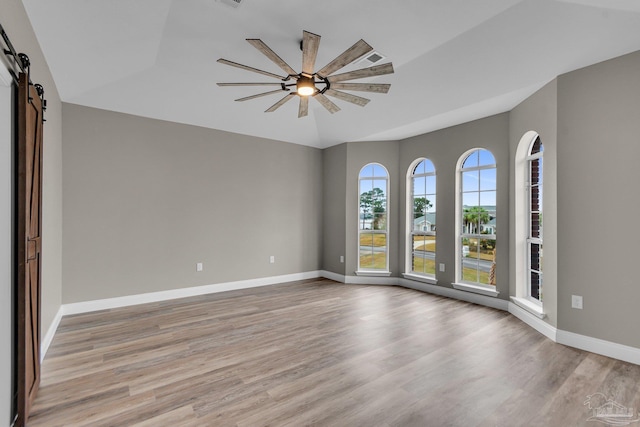 unfurnished room with a barn door, ceiling fan, and light wood-type flooring