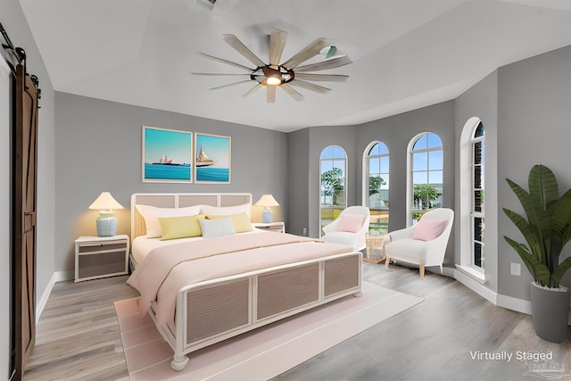 bedroom featuring a barn door, ceiling fan, and light wood-type flooring