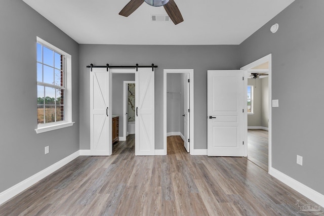 unfurnished bedroom with hardwood / wood-style floors, a spacious closet, ceiling fan, a barn door, and a closet