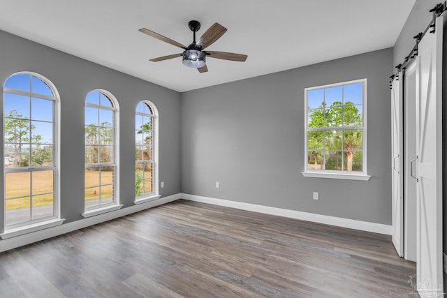 spare room featuring dark hardwood / wood-style flooring, a barn door, and ceiling fan