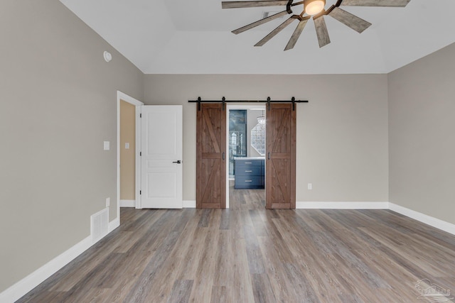 spare room featuring ceiling fan, a barn door, and light hardwood / wood-style floors