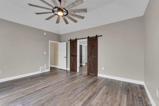 unfurnished bedroom featuring hardwood / wood-style flooring, vaulted ceiling, a barn door, and ceiling fan