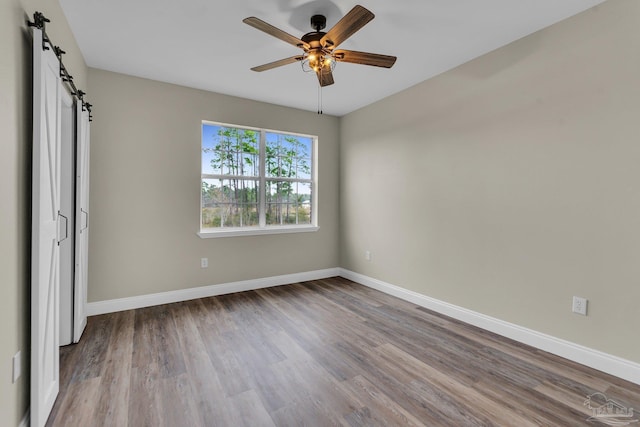 unfurnished bedroom featuring ceiling fan, a barn door, and light wood-type flooring